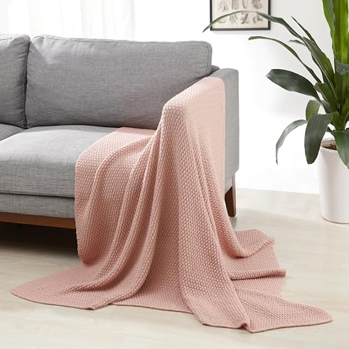 Manta decorativa rosa empolvada colocada en un sofá gris, ideal para decorar y proporcionar calidez.